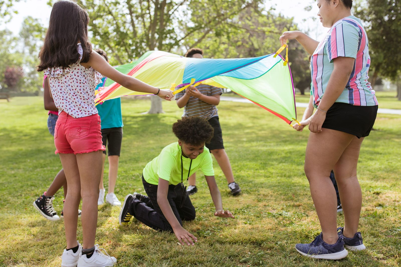Des enfants jouent ensemble en extérieur avec un parachute coloré lors d'une activité de vacances